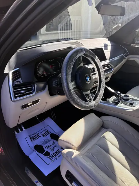BMW interior with cream leather seats after an interior detail, with a paper floor mat and steering wheel cover in place