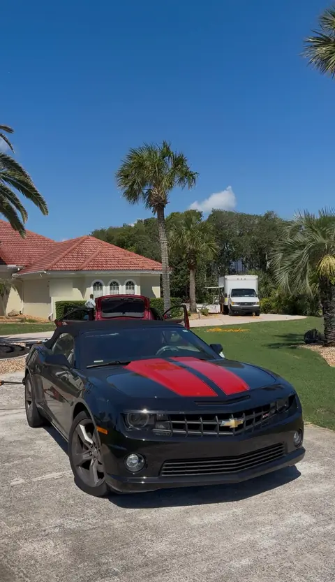 Black Chevrolet Camaro convertible with red stripes before an exterior detail, with brake dust darkening the wheels