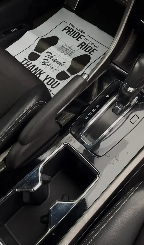 The same center console and cup holders cleaned after an interior detail, with a protective paper floor mat in place