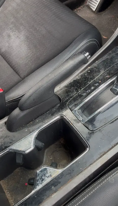 Dusty, stained center console and cup holders next to a cloth seat before an interior detail