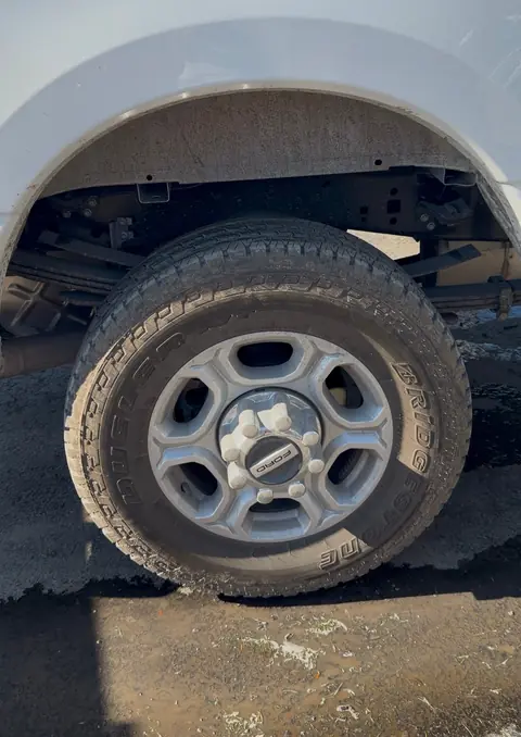 Mud-covered rear wheel, tire and wheel well on a white Ford Super Duty pickup before detailing
