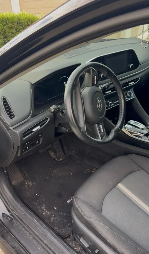 Hyundai Sonata driver's area before an interior detail, with a debris-covered floor mat and dusty steering wheel