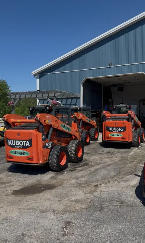 Three orange Kubota skid steers outside a shop after an equipment detail