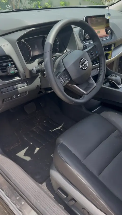 Nissan driver's area before an interior detail, with debris on the floor mat and dust on the dash and seat